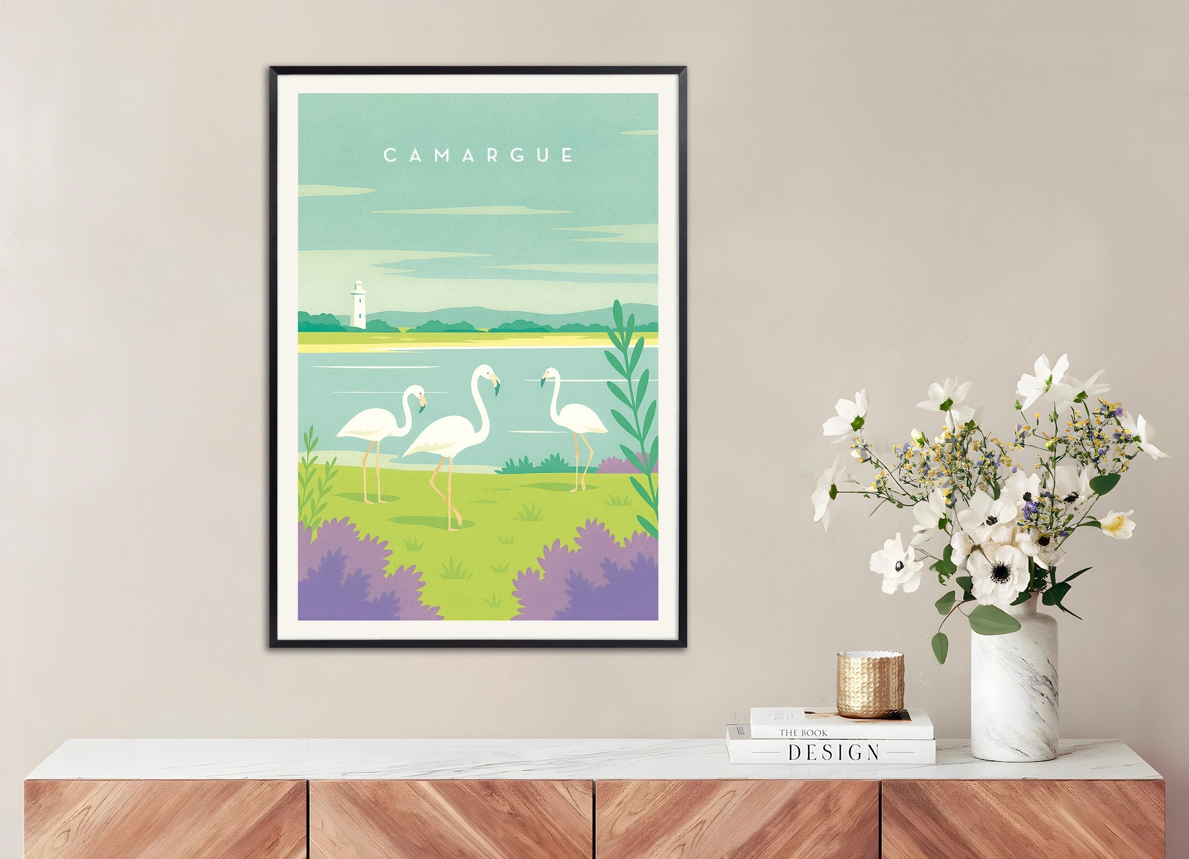 Framed artwork of flamingos in a natural setting on a wall above a wooden cabinet with a vase of flowers.