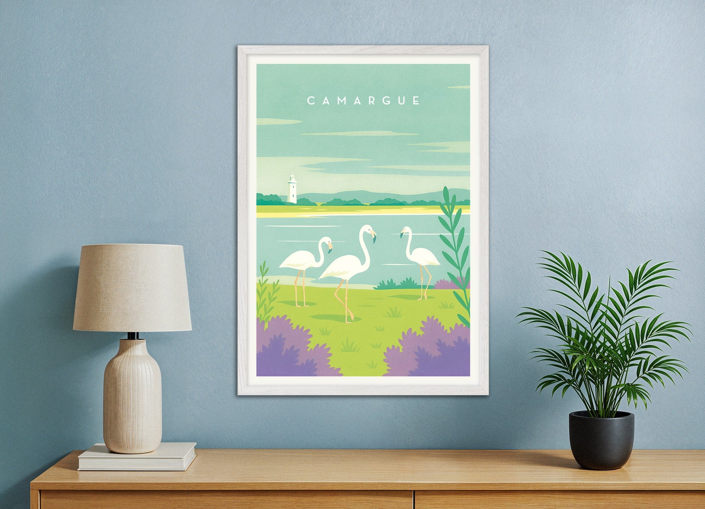Framed artwork of flamingos in a natural setting on a blue wall with a lamp and plant.
